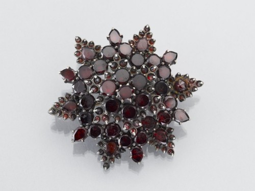 Stervormige broche van zilver, bezet met rode steentjes